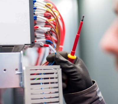 Closeup of electrician engineer works with electric cable wires of fuse switch box. Electrical equipment